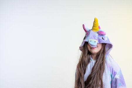 Waist up portrait of the young brunette girl in unicorn pajamas that pulled hood on her eyes, isolated over white background, copyspace for your textの写真素材