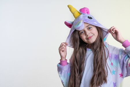 Sensual brunette girl with blue eyes and loose hair dressed in unicorn pajamas holds hood with her hands and looking at the camera isolated over white background, copyspace for your textの写真素材