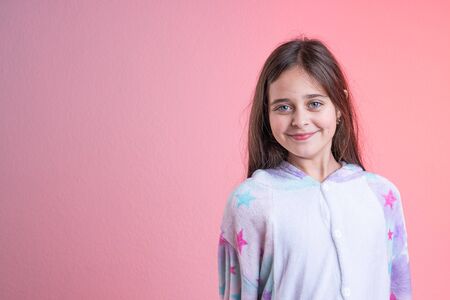 Waist up portrait of the beautiful brunette happy girl with blue eyes dressed in pajamas, looking at the camera, isolated over pink background, copyspace for your textの写真素材