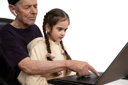Stylish old man in black hat and t-shirt teaches his granddaughter programming by using laptop, isolated over white backgroundの写真素材