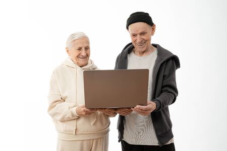 Couple of stylish seniors in casual clothes smiling and looking at the same laptop hugged isolated...