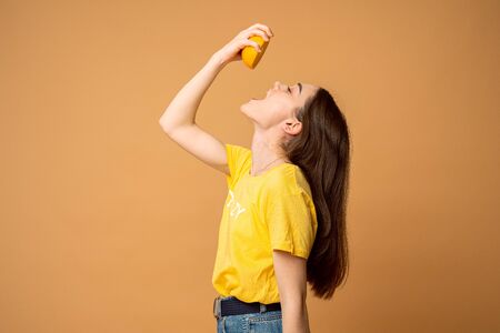 Brunette girl with closed eyes and loose hair dressed in yellow t-shirt holds half of orange ih her...