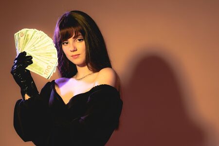 Portrait of a fashionable girl dressed in black retro dress holding bunch of money banknotes and...