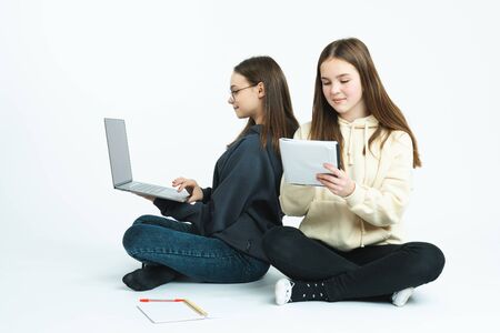 Two clever students in hoodies sitting togother on the ground with laptop and preparing for exams,...