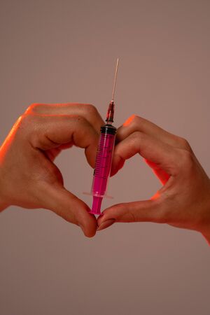 Close up photo, woman and man showing heart sign with pink syringe isolated over grey backgroundの写真素材