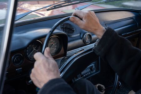 Unrecognizable man holding hands on steering wheel and driving retro car through country road at sunny autumn day. Guy controlling his auto riding at highway on high speed. Concept of road tripの写真素材
