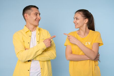 Image of happy young people man and woman in yellow shirts laughing and pointing fingers at each other isolated over yellow backgroundの写真素材