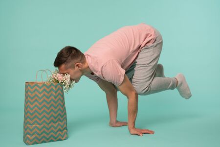 Young man in pink t-shirt standing in a hand stand, yoga pose and sniffing flowers from the shopping...