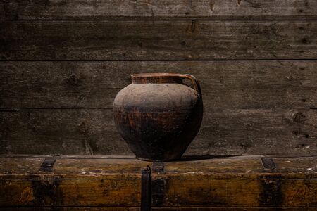 Ancient clay vase indoors with cold tones stands on wooden table, aged wooden wallの写真素材