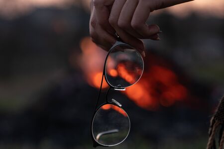Woman hands holding eyeglasses, you can see campfire through the glass of glasses, spring evening timeの写真素材
