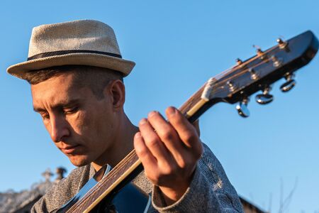 Music in nature, man wearing hat playing an acoustic guitar