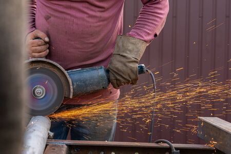 Close-up on the sides fly bright sparks from the welding machine. A young male welder in working...