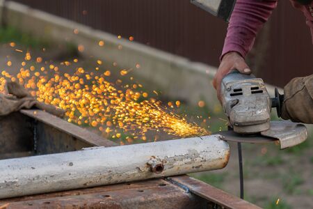 A young man welder processes a metal product with a angle grinder in the garage