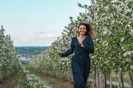 Happy attractive woman with loose hair wearing elegant green dress running along apple blooming gardenの写真素材