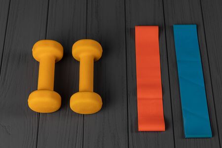 Multi-colored rubber bands for fitness and dumbbells isolated on grey background