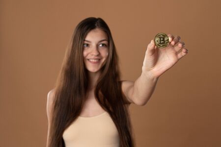 Happy girl eith brunette lose hair holdsd bitcoin golden coin in her hand, focus on the coin, girl is blurredの写真素材