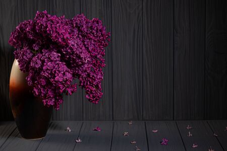 Bouquet of pink lilac flovers in vase on wooden table with fallen petalsの写真素材