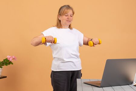 Woman using laptop at home watching fitness videos online workout class training with yellow...
