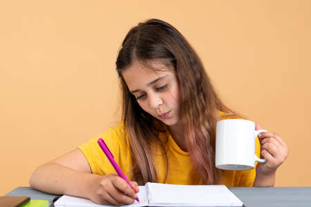 Student makes a note in a notebook reading a book at home at a table