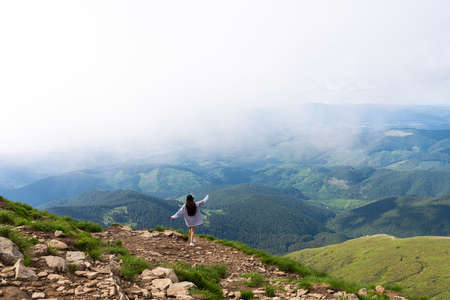 The girl stands on top of the mountain and enjoys the view of the valley. At the dawn, hands upの写真素材