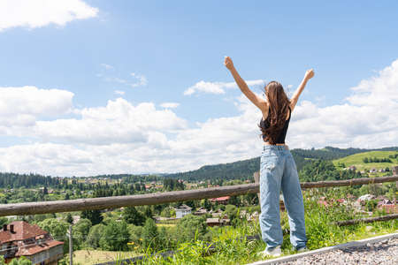 Woman traveler standing with hands up achieving the top of mountainsの写真素材