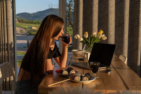 Happy woman holding glass with red wine near tasty sushiの写真素材