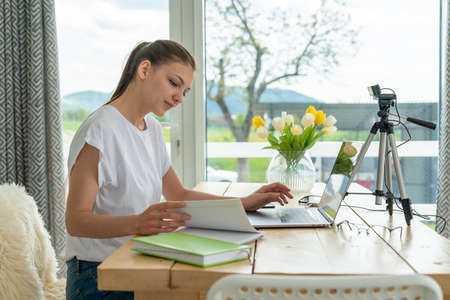 Focused young freelance woman sitting on the table at home with laptop, working remotely online from homeの写真素材