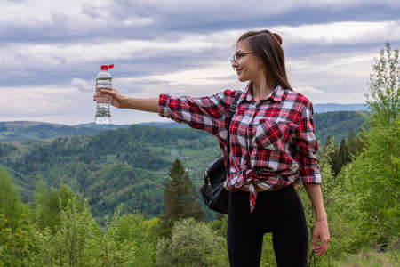 Girl trekking outdoors on the mountains, she is holding a water bottle and carrying a backpack with hiking poleの写真素材