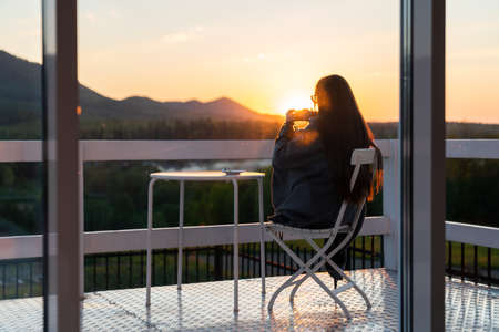 Young woman traveler holds cup of tea in her hands at mountain resortの写真素材
