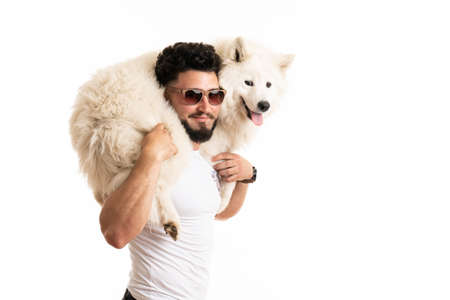 Stylish bearded man in glasses holds samoyed dog on his back, smiling and looking at the cameraの写真素材