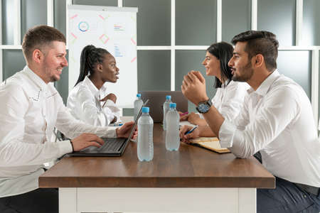 Group of smiling multicultural business partners sitting at table with laptops and papersの写真素材