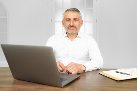Middle age handsome businessman wearing tie sitting using laptop at the office with serious expression on face. Simple and natural looking at the cameraの写真素材