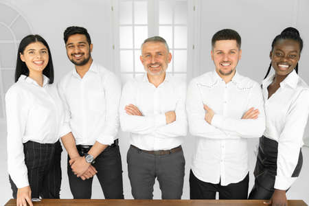 Portrait of standing in row smiling diverse team posing, all in white shirts. Happy young...