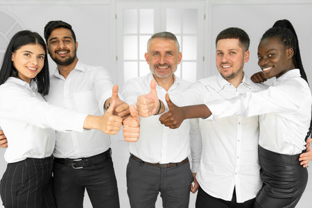 Group of happy smiling international office workers in white shirts showing thumbs up and looking at the cameraの写真素材