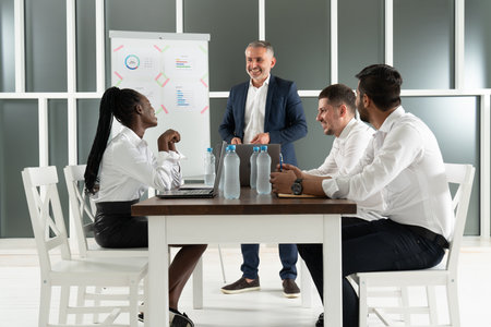 Group of a young international office employees dressed casually in the suits having some office work at the large meeting table in the bright sunny roomの写真素材