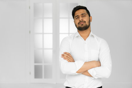 Indian handsome young man in white shirt standing with hands folded against white backgroundの写真素材