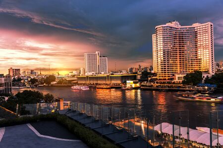A large building in the city by the river at sunset that reflects beautiful light and water travel.の写真素材