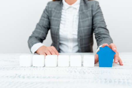 A Lady Holding Home In Business Outfit Presenting Possibility Of Owning Your Own Real Estate. Buying House Or Moving New Insurance Or Mortage Concept Shown By The Young Businesswoman.の写真素材