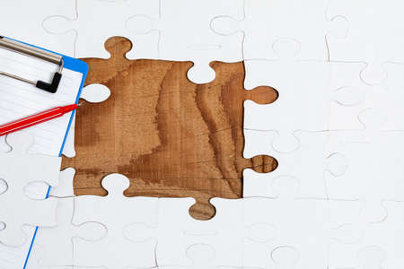 Close-Up White Jigsaw Pattern Puzzle Pieces To Be Connected With Missing Last Piece Positioned On A Flat Lay Background With Different Texture And Paper Supplies Accesoriesの写真素材