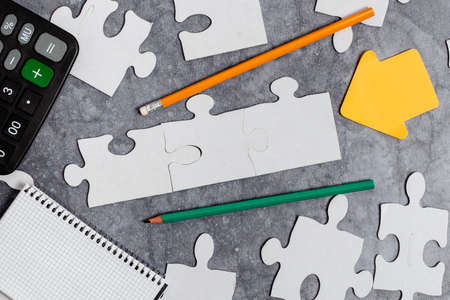 Close-Up White Jigsaw Pattern Puzzle Pieces To Be Connected With Missing Last Piece Positioned On A Flat Lay Background With Different Texture And Paper Supplies Accesoriesの写真素材