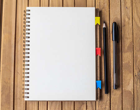 Empty Opened Clipped Journal Beside Pens On Top Of The Wooden Desk. Blank Open Notepad With Clip And...