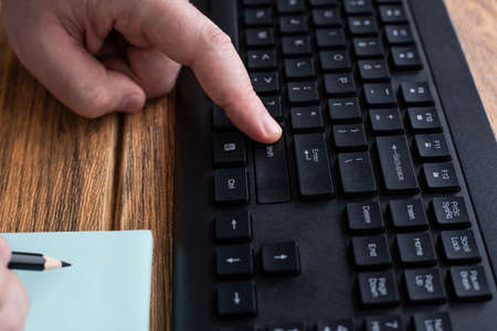 Hands Pressing Computer Keyboard Keys While Writing With Pencil In Notepad. Palms Typing Notebook...