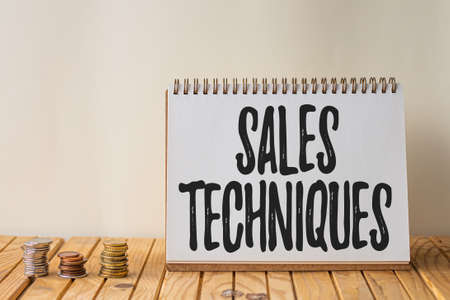 Conceptual caption Sales Techniques. Business concept methods that sales professionals use to create revenue Empty Open Spiral Notebook Beside Stockpile Of Coins On Top Of Desk.の写真素材