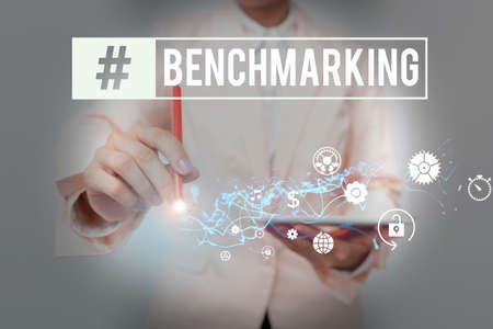 Sign displaying Benchmarking. Internet Concept evaluate something by comparison with standard or scores Lady In Suit Holding Phone And Performing Futuristic Image Presentation.の写真素材