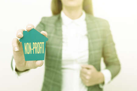 Handwriting text NonProfit. Business concept not making or conducted primarily to make profit organization A Young Lady Businesswoman Holding Presenting Home In Business Outfitの写真素材