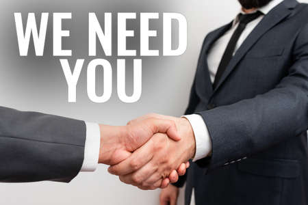 Sign displaying We Need You. Word Written on asking someone to work together for certain job or target Two Professional Well-Dressed Corporate Businessmen Handshake Indoorsの写真素材