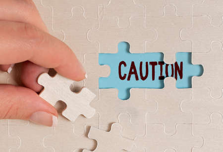 Conceptual caption Caution. Business approach Care taken to avoid danger or mistakes Warning sign Prevention Building An Unfinished White Jigsaw Pattern Puzzle With Missing Last Pieceの写真素材
