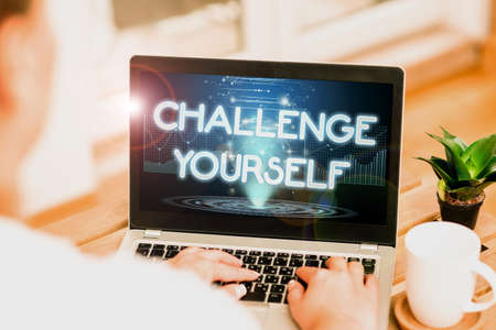 Conceptual caption Challenge Yourself. Word for Setting Higher Standards Aim for the Impossible Woman Busy Typing On Laptop Beside Coffe Mug And Plant Working From Home.の写真素材