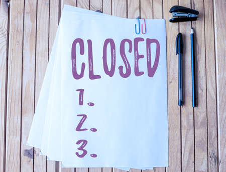 Sign displaying Closed. Word Written on Finished and therefore not able to be discussed any more Not open Office Stationery Paper Clipped Together Laying Flat On Table.の写真素材