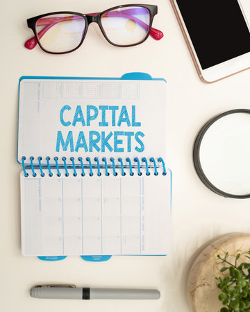 Handwriting text Capital Markets. Concept meaning Allow businesses to raise funds by providing market security Office Supplies Over Desk With Keyboard And Glasses And Coffee Cup For Workingの写真素材